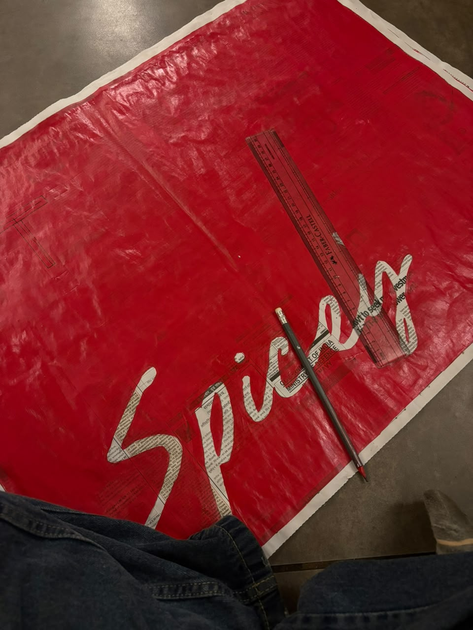 Hand-cut red tote stencil of the Spicey script wordmark with ruler and pencil