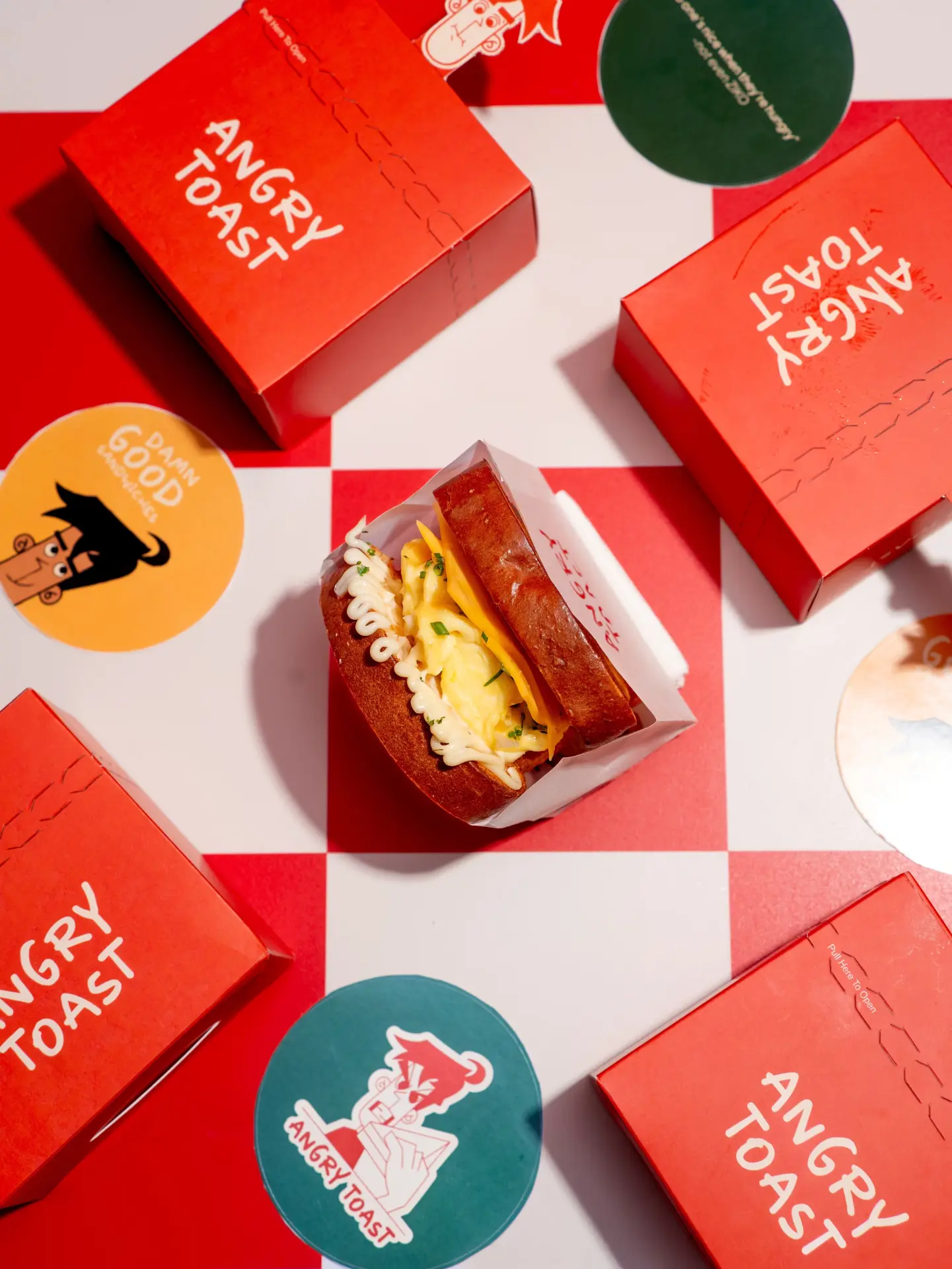 Angry Toast takeaway boxes and stickers on a red checkerboard surface