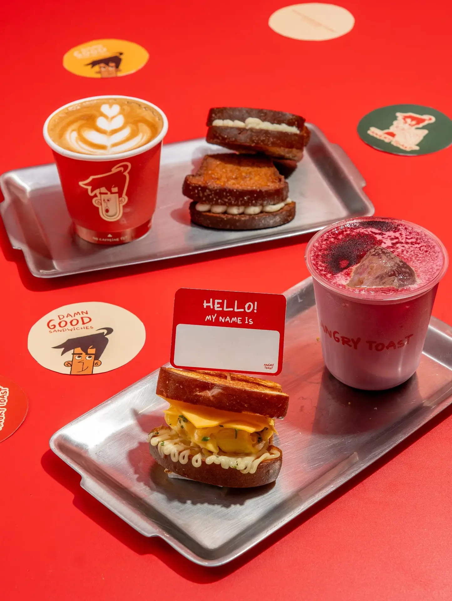 Metal trays with a latte, toasted sandwiches and a Hello my name is card on red