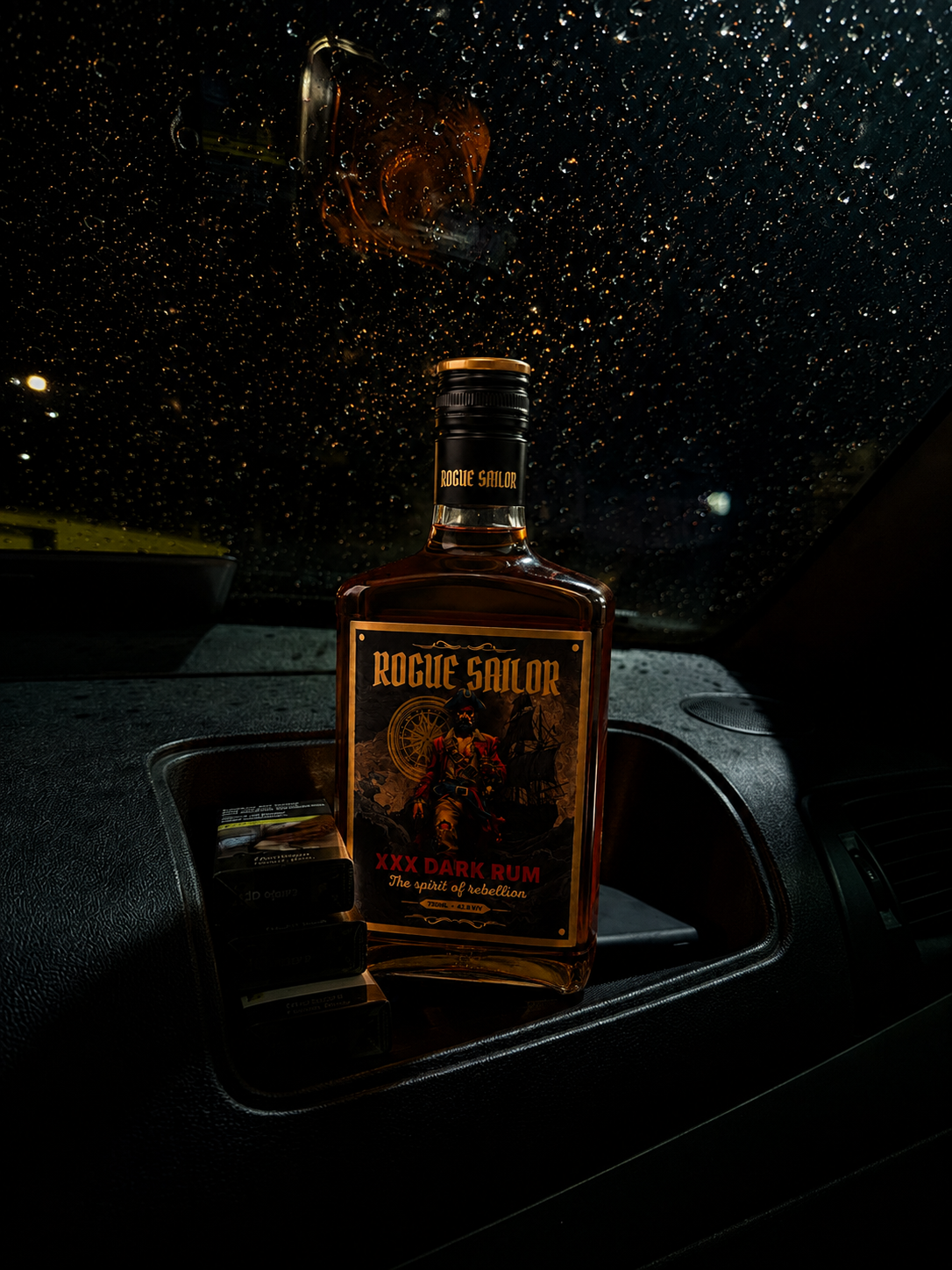 Rogue Sailor bottle on a car dashboard at night with rain on the windshield