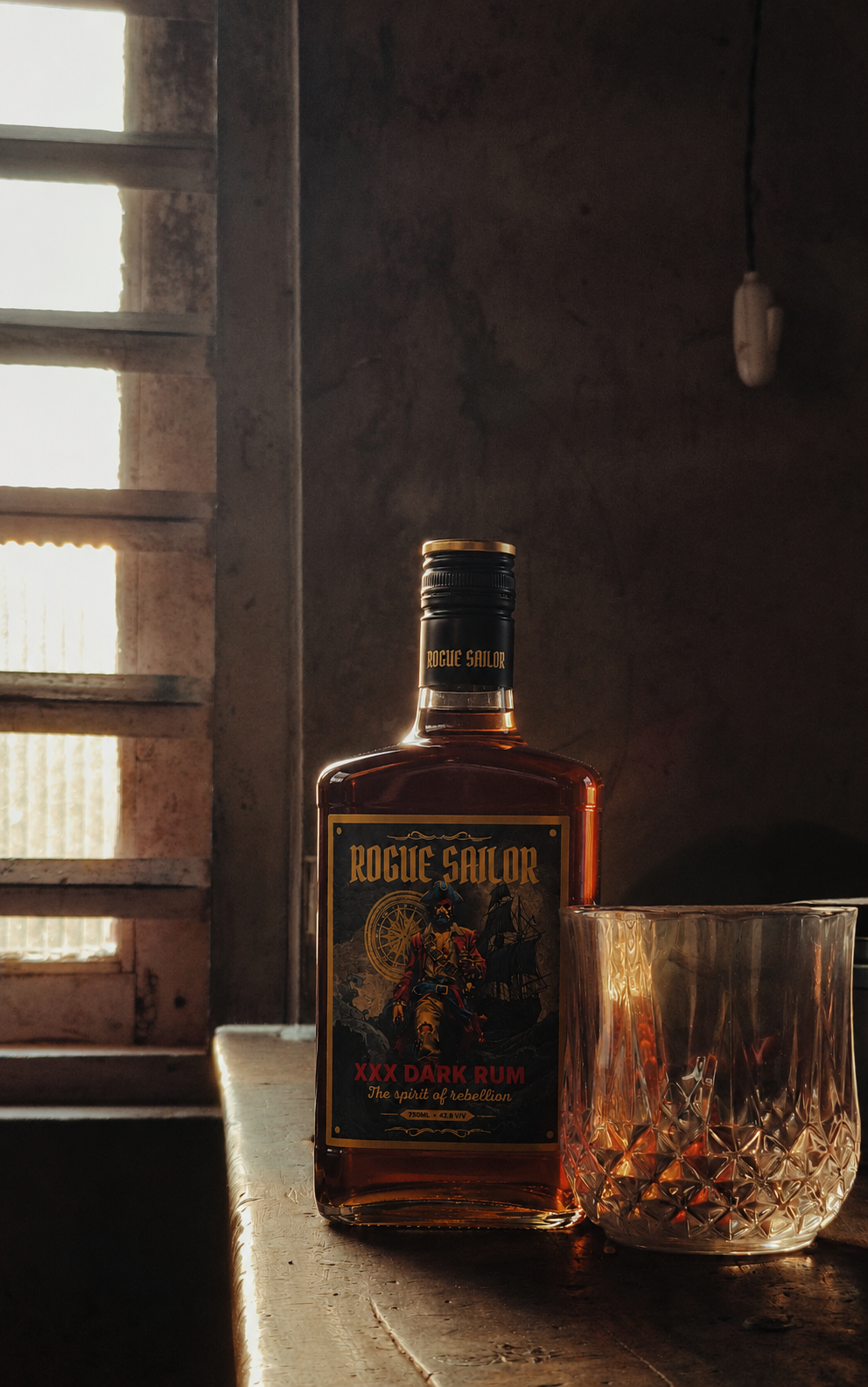 Rogue Sailor bottle and cut-glass tumbler on a weathered table beside a sunlit window